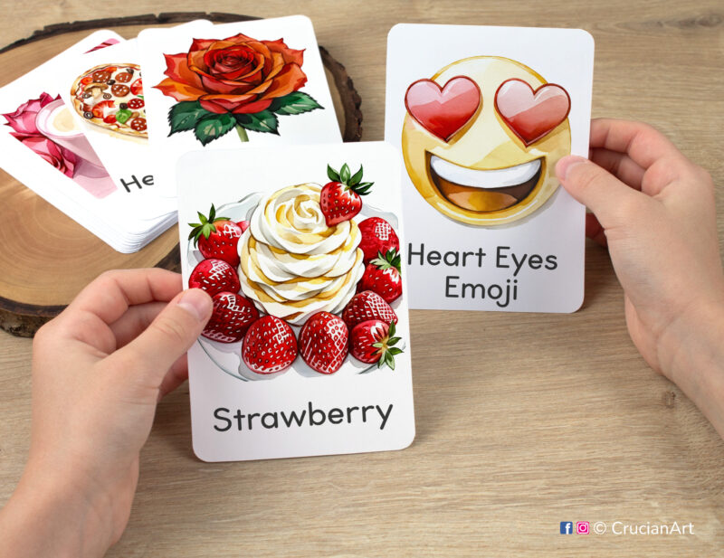 Preschooler hands holding Saint Valentine Day flashcards with watercolor images of Strawberries and Heart Eyes Emoji