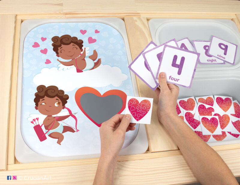 Toddler sensory play: Valentine's Day African American Cupid worksheet for a holiday educational activity inserted into IKEA Flisat table, with red hearts counters placed in the Trofast box.
