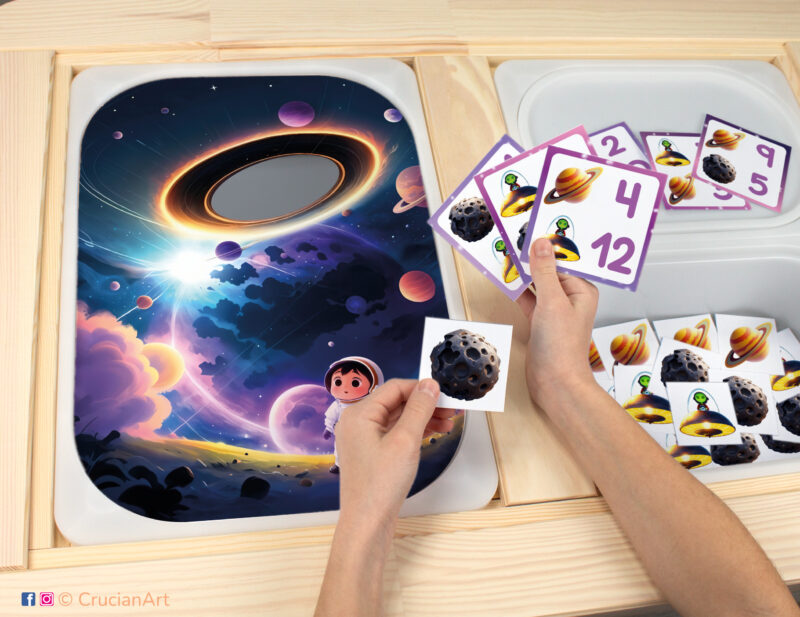 Toddler sensory play: Outer Space Black Hole worksheet for an educational activity inserted into IKEA Flisat table, with asteroids and planets counters placed in the Trofast box.