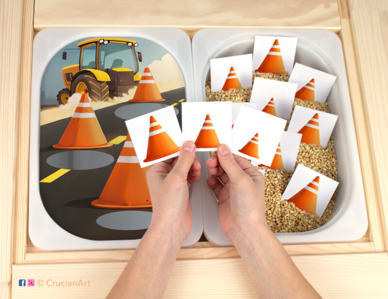 The Construction theme preschool pretend play setup features a sorting by size activity. Children's hands holding cards with large, medium, and small traffic cones.