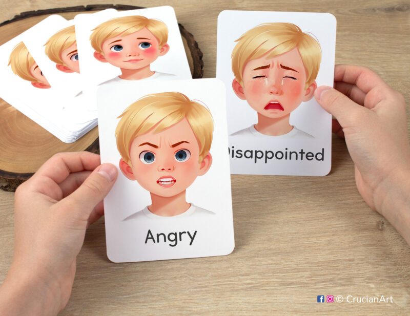 Preschooler hands holding flashcards with watercolor images of Angry and Disappointed boy faces. Emotions and Feelings flash cards for boys with fair hair and skin.