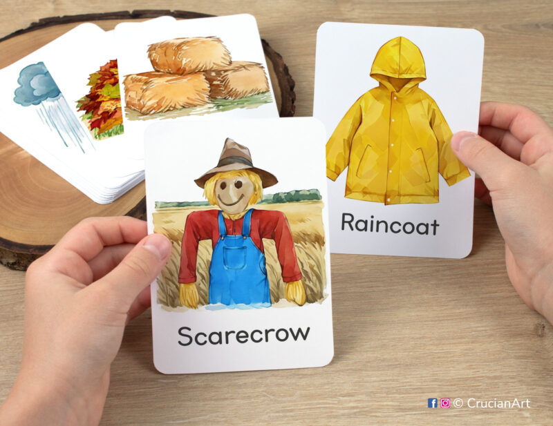 Watercolor illustrations of Scarecrow and Raincoat flashcards in kindergartener's hands. Printable learning materials for Autumn Harvest and Falling Leaves study units.