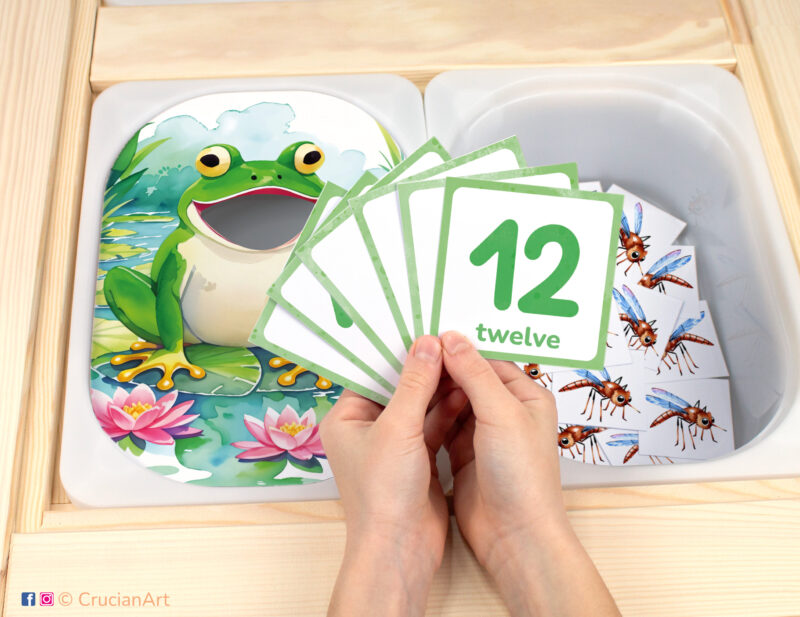 On the Pond pretend play setup for Spring and Summer Season theme counting game. Froggy themed sensory table insert and kids' hands holding task cards displaying numerals from 1 to 12.