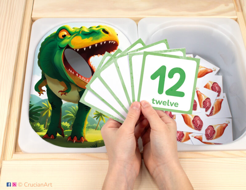 Tyrannosaurus Rex pretend play setup for a Dinosaur theme counting game. T-Rex Dino themed sensory table insert and kids' hands holding task cards displaying numerals from 1 to 12.