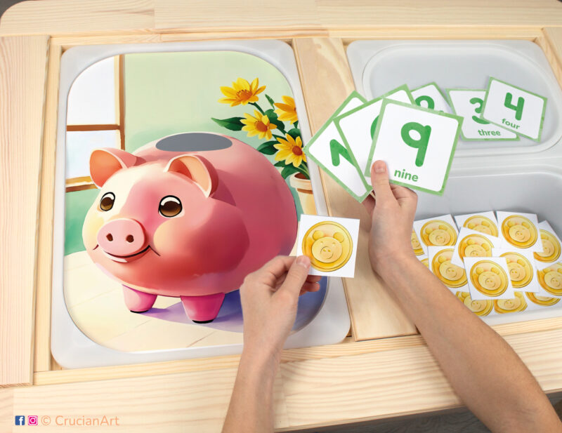 Toddler sensory bins play: Pink Piggy Bank worksheet for an educational activity. DIY template inserted into IKEA Flisat table, with gold coins counters placed in the Trofast box.
