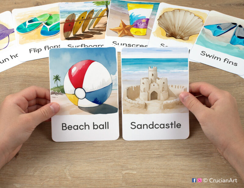 Preschooler's hands holding flashcards with watercolor images of Beach Ball and Sandcastle. Sunny season Montessori printables.