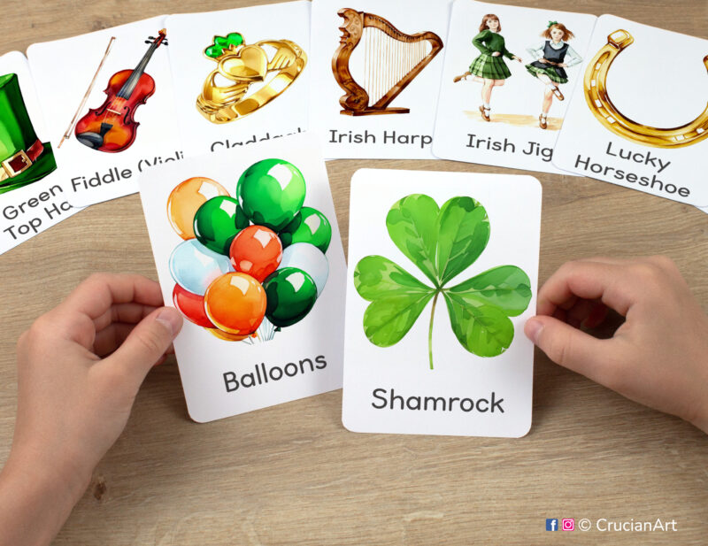 Preschooler's hands holding flashcards with watercolor images of Shamrock and Green Balloons.