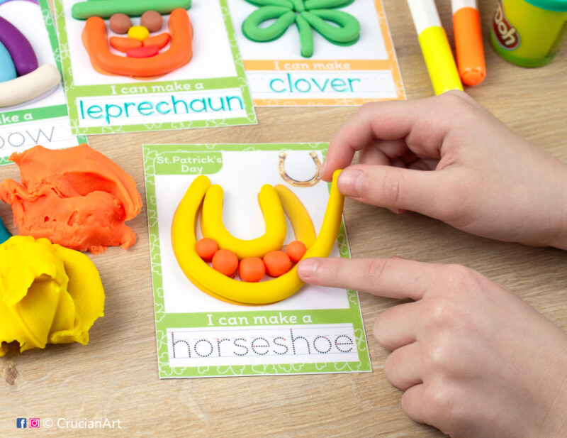 A preschooler is playing with play-doh, molding a Saint Patrick Day themed Lucky Horseshoe. Montessori-inspired playdough mats for toddlers fine motor skill development.