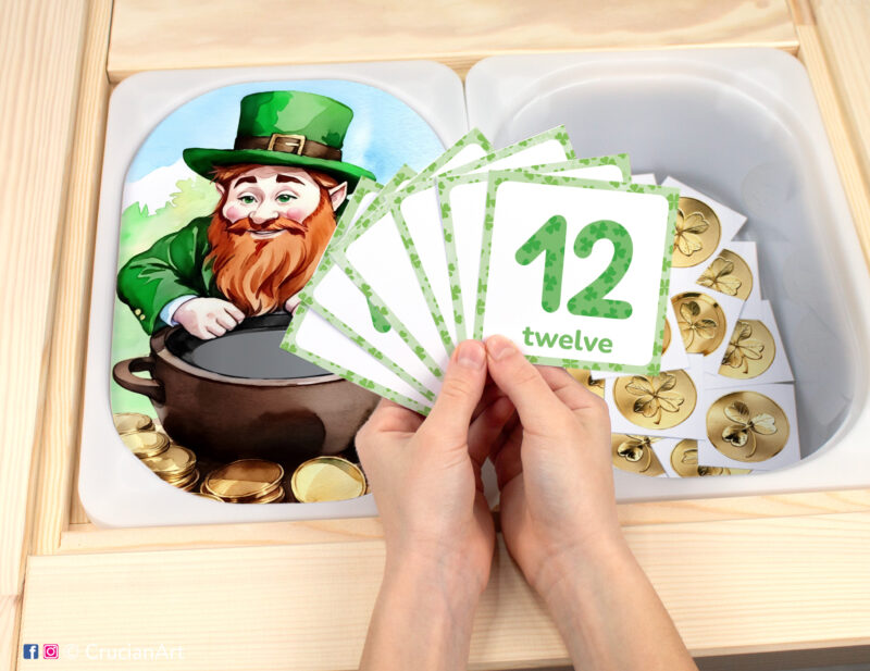 Leprechaun pretend play setup for a St. Patrick's Day counting game. Kids' hands holding task cards displaying numerals from 1 to 12.