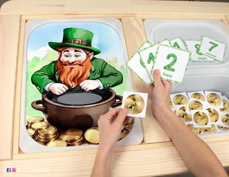 Toddler sensory play: Patrick's Day Leprechaun worksheet for an educational activity inserted into IKEA Flisat table, with gold coins counters placed in the Trofast box.