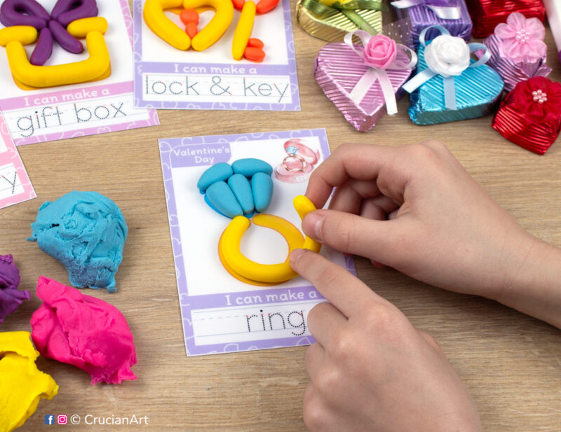 A preschooler is playing with play dough, molding a Saint Valentine Day themed ring. Montessori-inspired playdough mats for toddlers fine motor skill development.