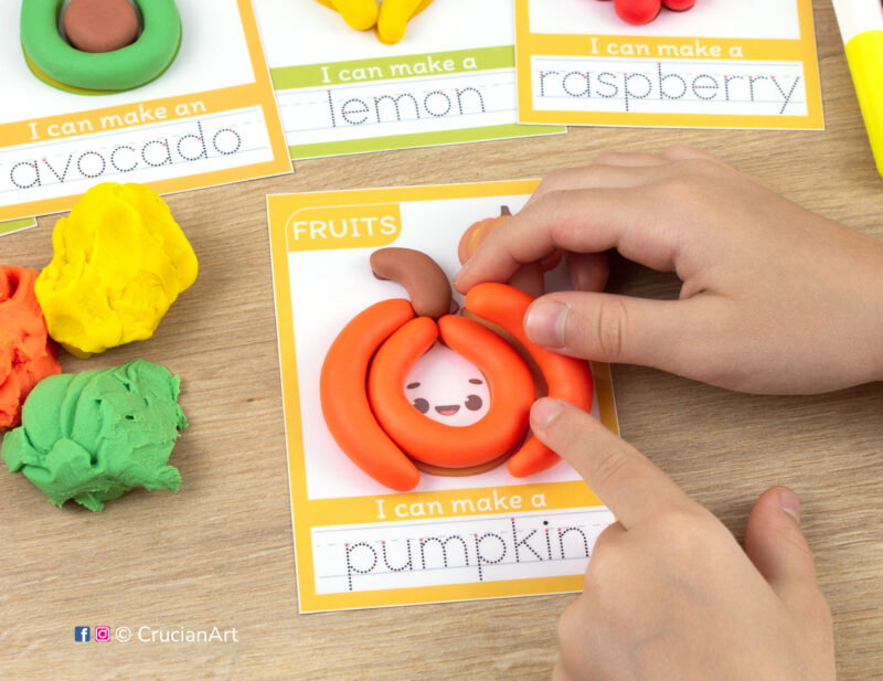 A preschooler is playing with play-doh, molding a pumpkin. Fruits and veggies playdough mats for toddlers fine motor skill development.