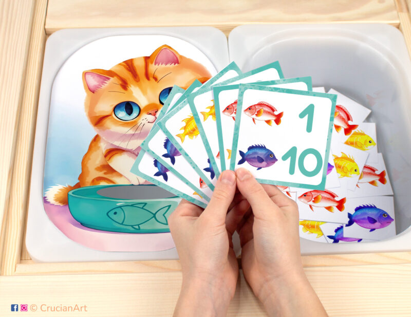 Feed the Hungry Kitten Fish pretend play setup for a matching and counting game. Kids' hands holding task cards displaying numerals and fish. Pets unit printables for toddlers.