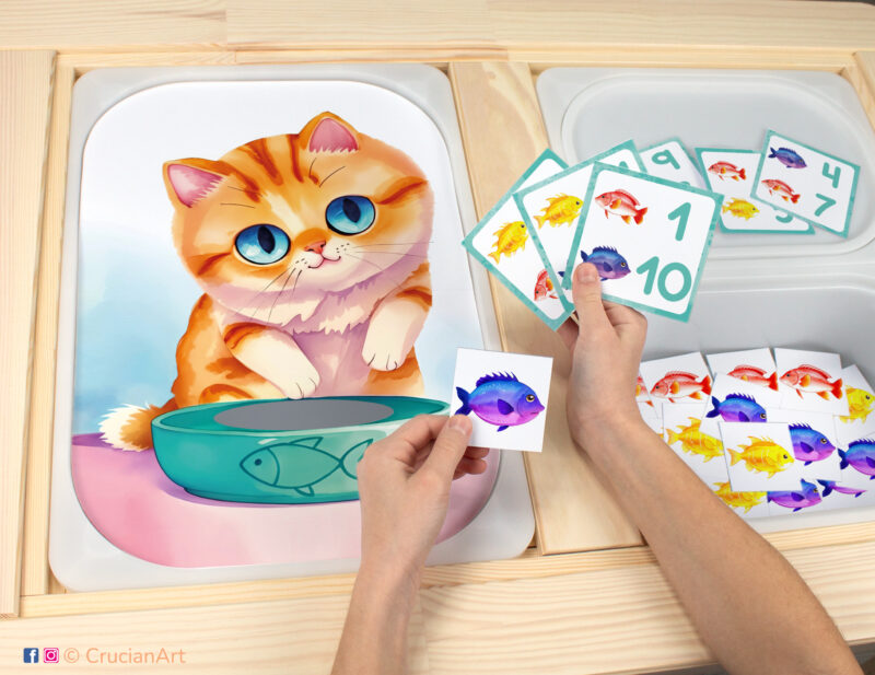 Toddler sensory play: Hungry Kitten worksheet for an educational counting activity inserted into IKEA Flisat table and counters with fish placed in the Trofast bin.
