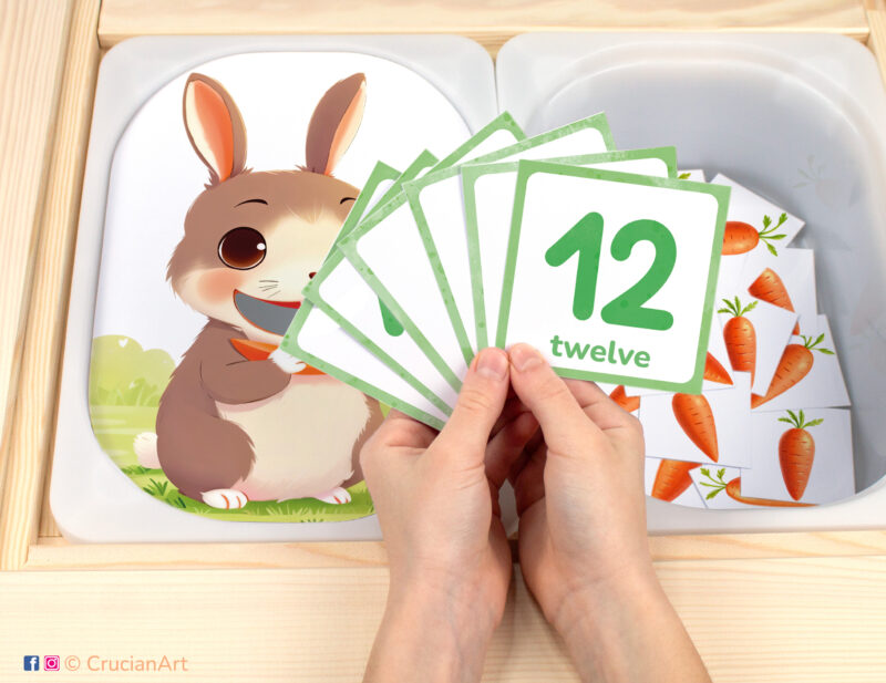 Feed the bunny carrots pretend play setup for a spring counting game. Sensory table insert and kids' hands holding task cards displaying numerals from 1 to 12.