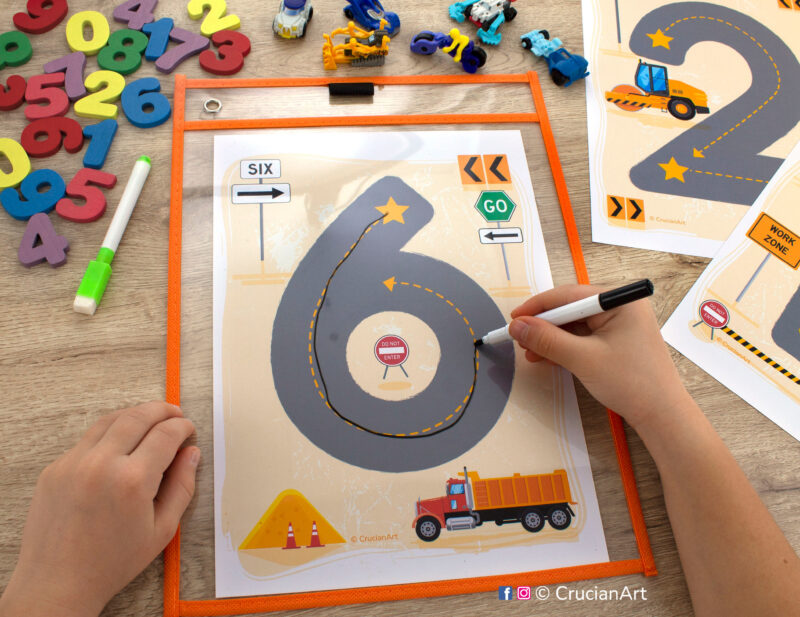 Number mat placed into a dry erase pocket sleeve. Preschooler writing number six with a dry erase marker. Construction trucks theme printables for toddler and preschool curriculum.