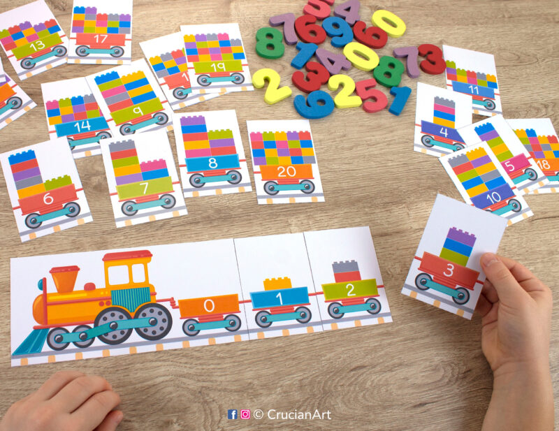 Number train learning activity for kids. Toddler holding a card showing a train carriage with three bricks and numeral 3. Preschool printables for early learning.