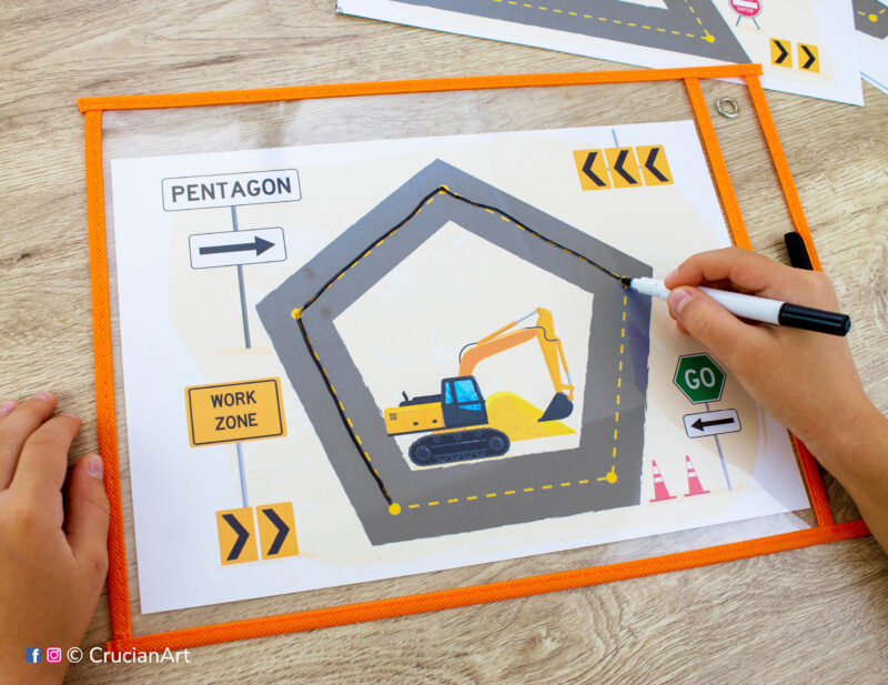 Two-dimensional shape worksheets placed into a dry erase pocket sleeve. Preschooler tracing a pentagon shape with a dry erase marker. Construction trucks theme printables for toddler and preschool curriculum.