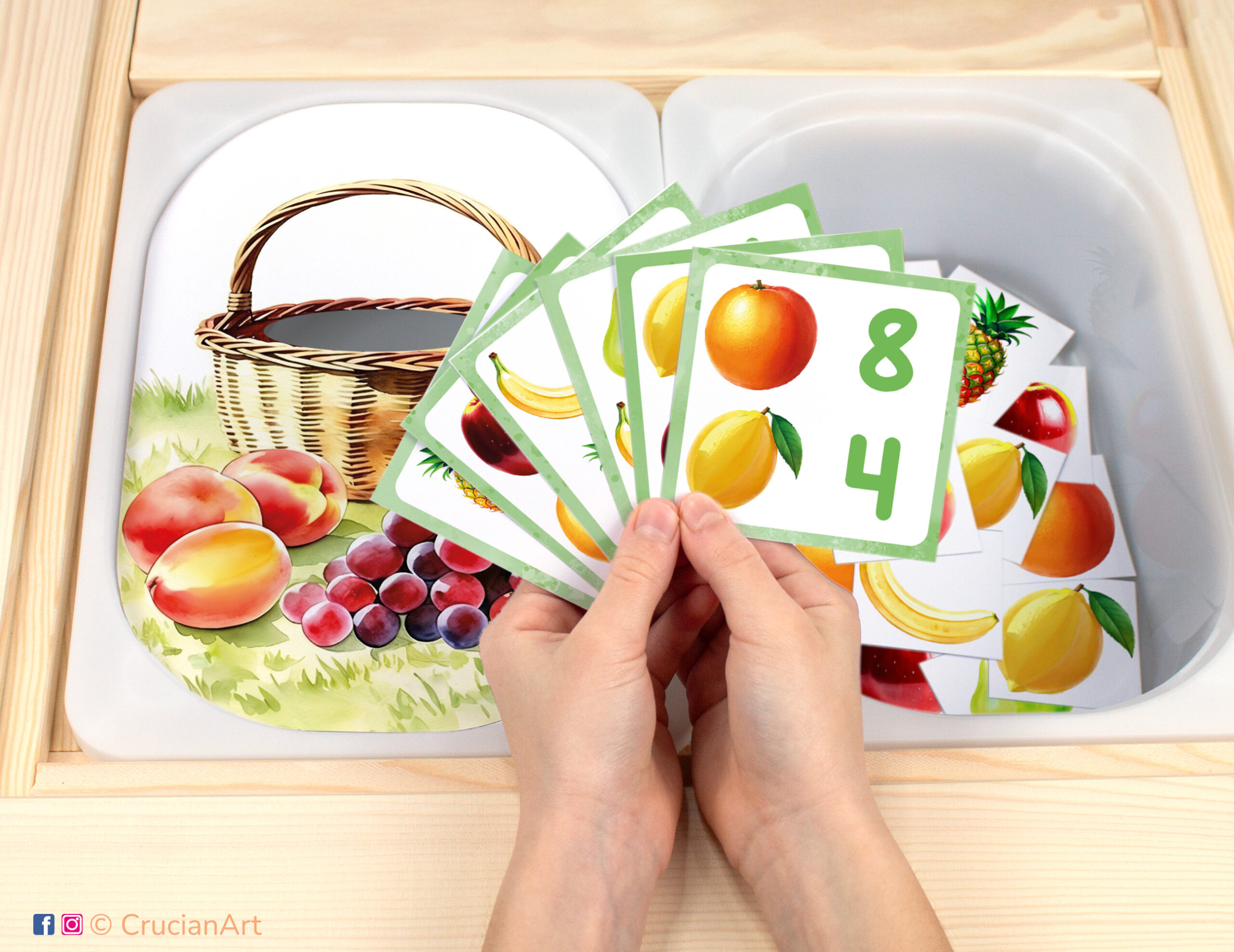 Harvest time pretend play setup for a matching and counting game. Kids' hands holding task cards displaying numerals and apple, banana, orange, pineapple, pear, lemon. Fruits unit printables for toddlers.