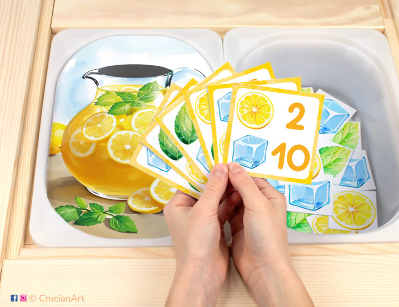Lemonade recipe pretend play setup for a matching and counting game. Kids' hands holding task cards displaying numerals and lemon slices, mint leaves, ice cubes. Summer fruits unit printables for toddlers.