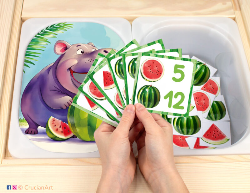 Feed the hippo pretend play setup for a matching and counting game. Kids' hands holding task cards displaying numerals and watermelon slices. Zoo animals unit printables for toddlers.