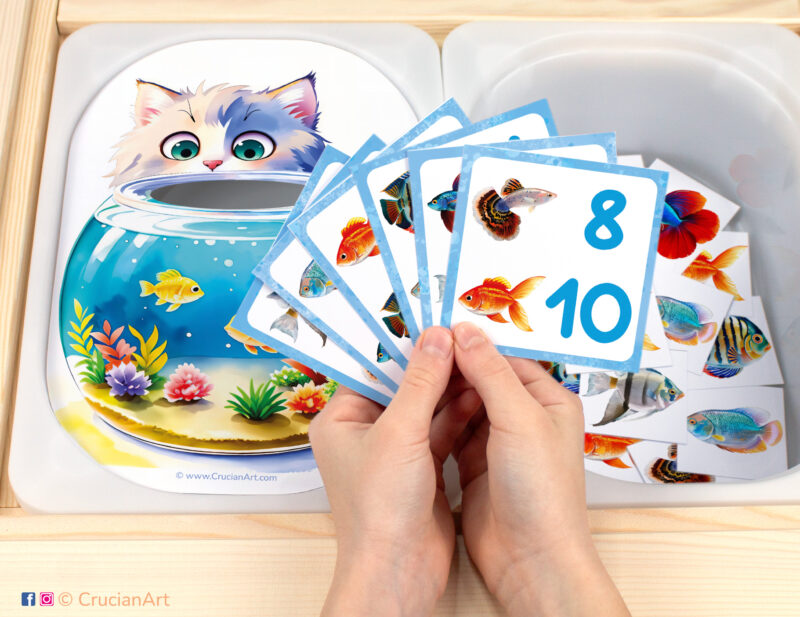 Fill the fish tank pretend play setup for a matching and counting game. Kids' hands holding task cards displaying numerals and goldfish, betta fish, discus fish, angelfish, guppy and gourami. Aquarium fish printables for the pet theme unit.