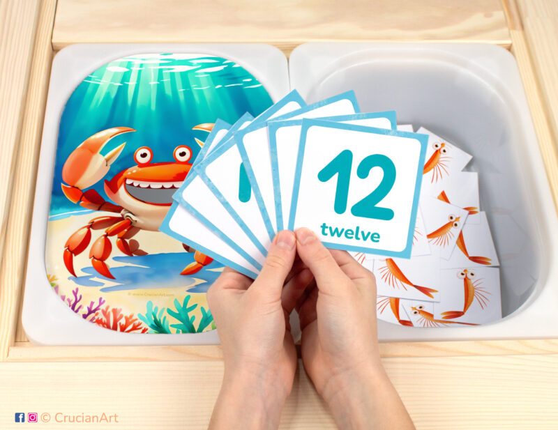 Feed the crab plankton pretend play setup. Sensory table insert and kids hands holding task cards displaying numerals from 1 to 12. Printable activity for under the sea unit.