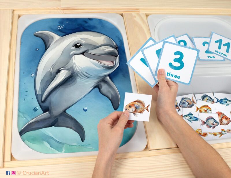 Feed the Dolphin fish counting game for toddlers: ocean animals theme worksheet for an educational activity. DIY template inserted into ikea flisat table, with counters placed in the trofast bin.